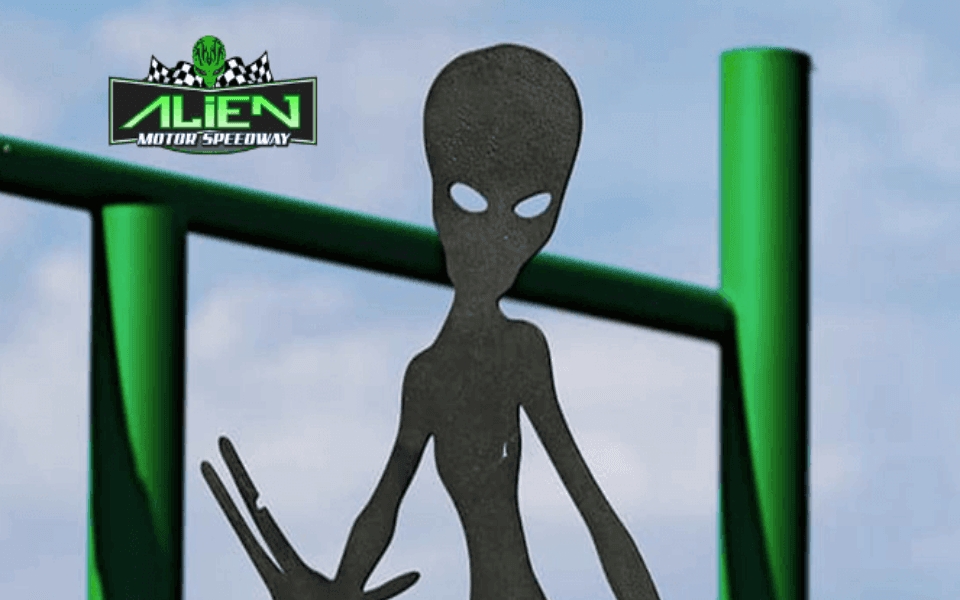 An alien holding out its hand in front of a green alien motor speedway logo