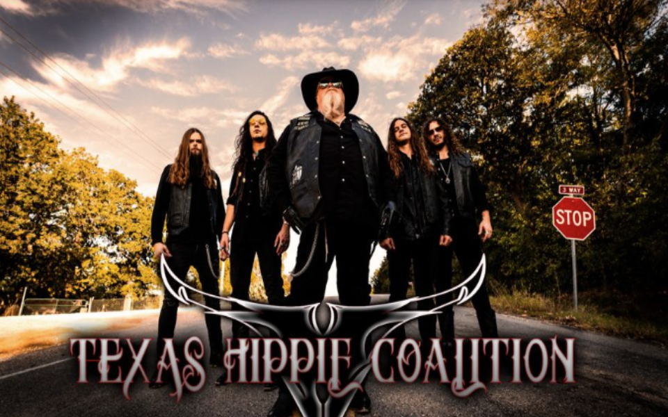 Texas Hippie Coalition members standing in the middle of a road with a stop sign on the right and trees to both sides